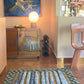 Pyrus Stripe Rug in Low Tide – hand-knotted studio-designed rug in green and blue installed in a kitchen with a mirror-front cabinet, a spherical lamp, a wine rack, a modern chair, and a painting of a flying bird on the wall | Eskayel  
