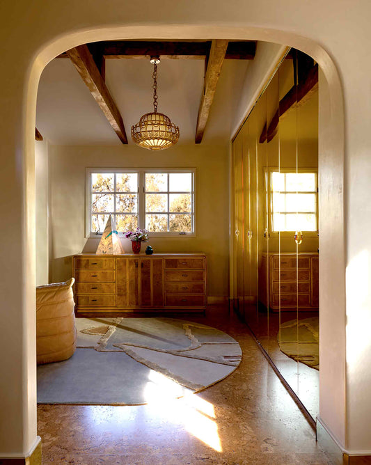 Pieces Rug in Mineral in a room – hand-knotted studio-designed rug in a multicolor palette installed in a living room with an Archway leading into the room with warm-toned wooden furniture and a chandelier| Eskayel