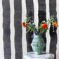 A vase of flowers on a table in front of a black and white striped Bold Stripe Grasscloth Slate wall