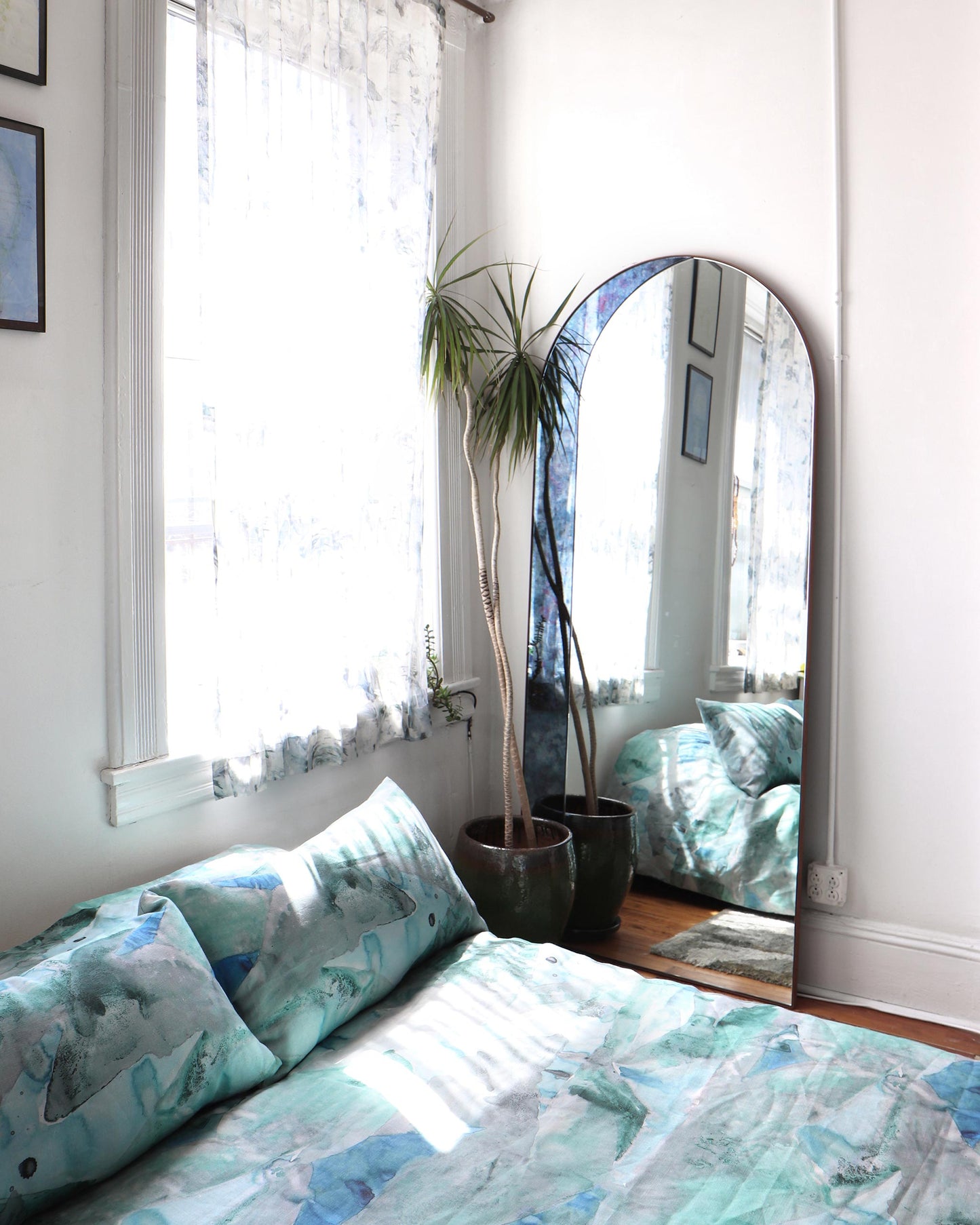A small bedroom with a Mani Fabric||Gulf bed and a mirror in turquoise colorway.