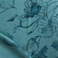 A close up of a teal fabric with Belize Blooms Fabric Aquamarine flowers on it