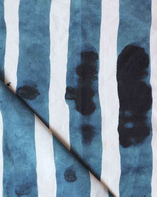 A blue and white striped Bold Stripe Fabric Azure with black splotches from the Stripes Collection