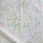 A white fabric with green and purple flowers, Bosky Toile Fabric Cay, on it