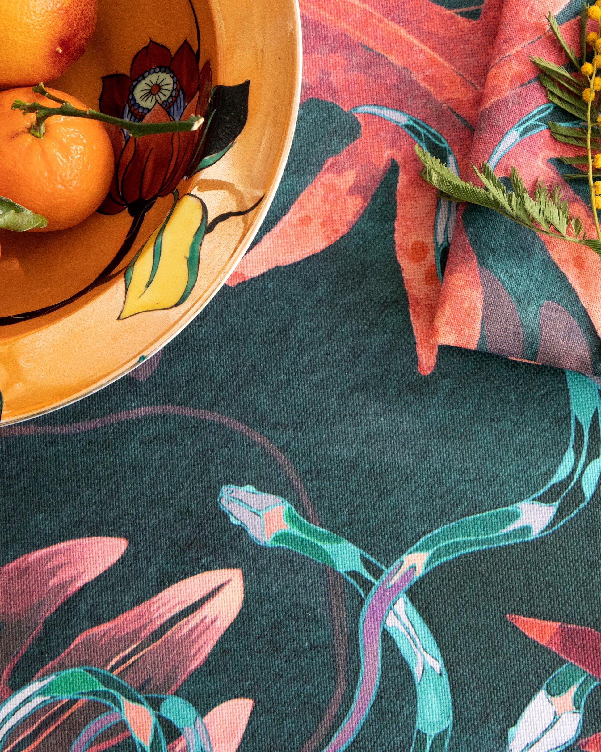 A bowl of oranges on a table with an Edera Fabric Beryl tablecloth