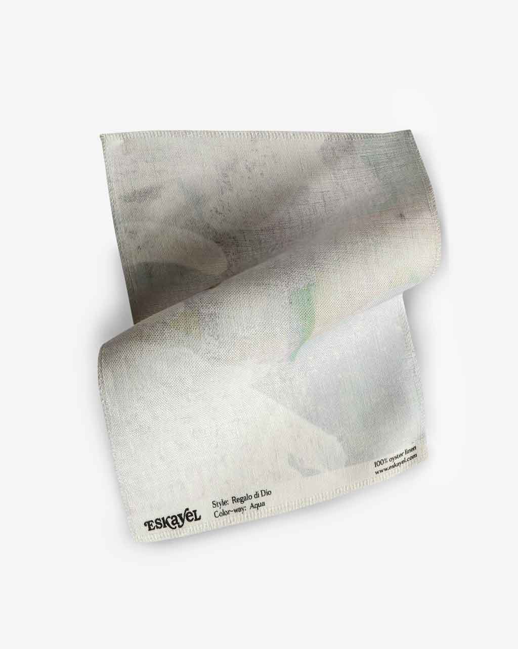 A white napkin on a Regalo di Dio Fabric Aqua surface