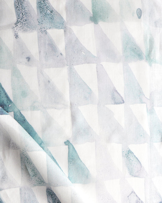 A close up of Triangle Checks Fabric||Verde, a white fabric with a geometric pattern.