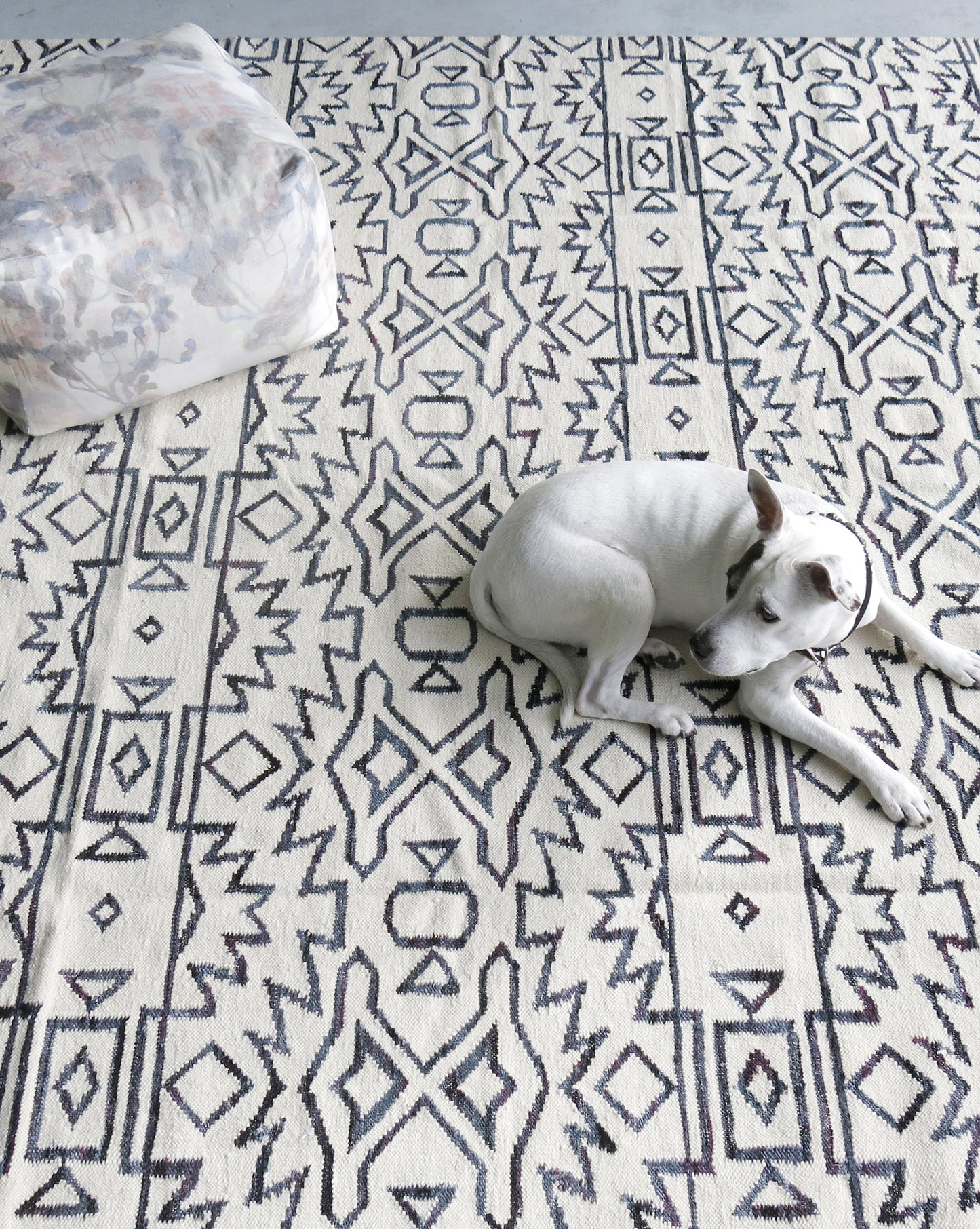 A dog laying on an Akimbo 5 Flatweave Rug Black And White with a geometric pattern