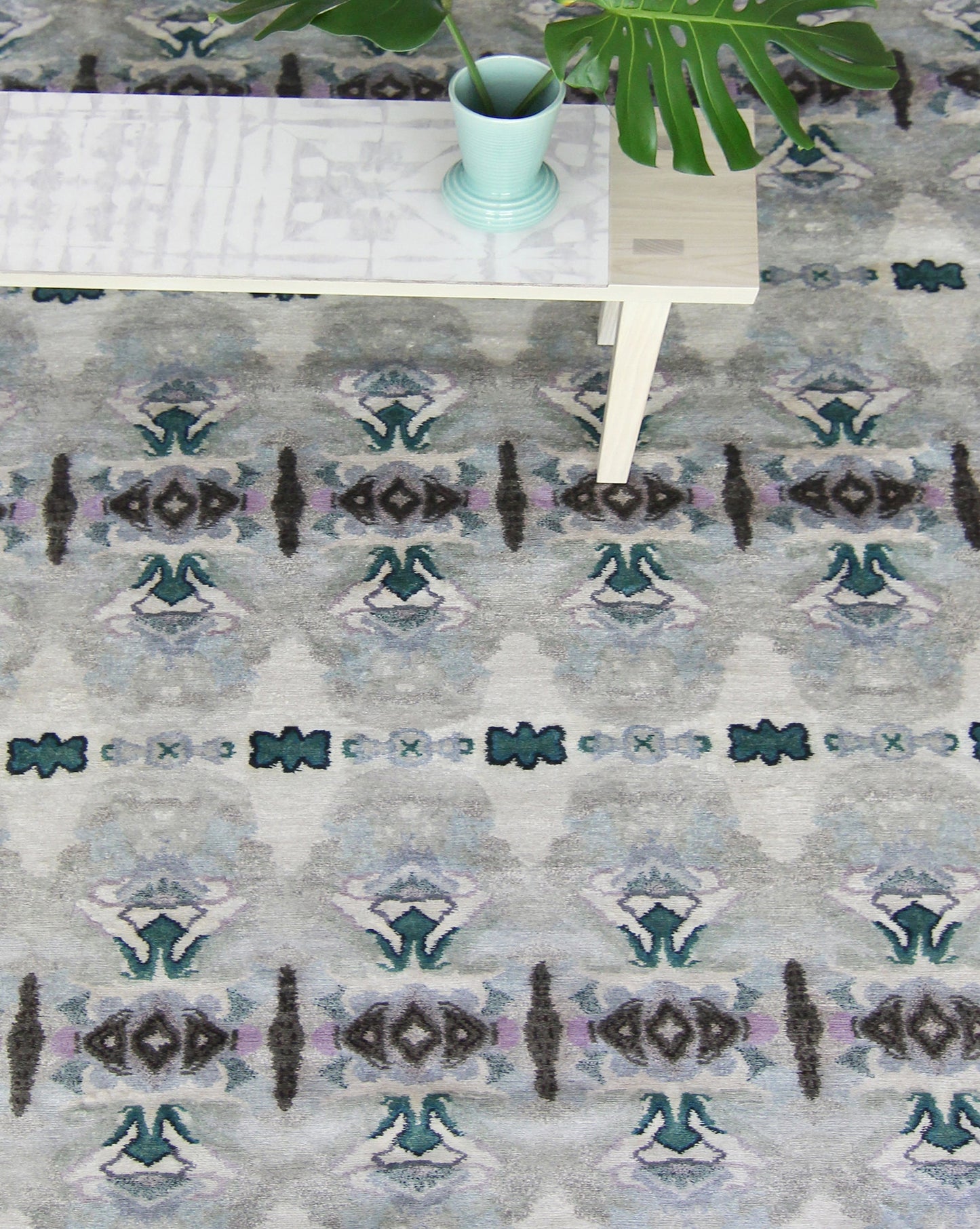 A table with a Septaria Hand Knotted Rug Light on it next to a rug showcasing beautiful colors