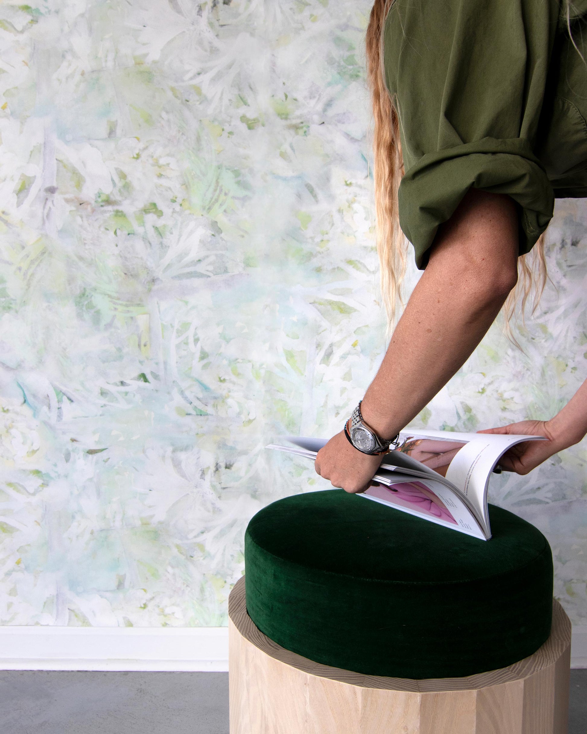 A woman is reading a book on a Cortile Wallpaper Luminosa stool