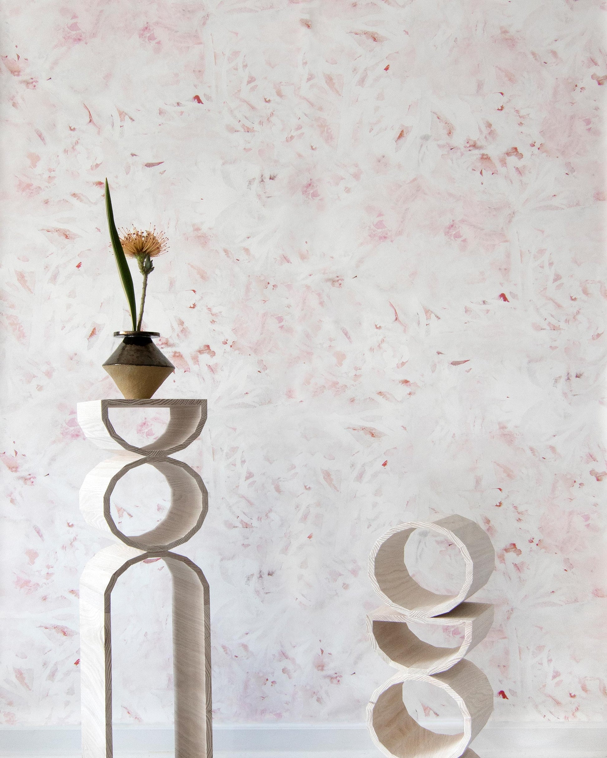 A pink and white Cortile Wallpaper Pelle wall with a vase in front of it