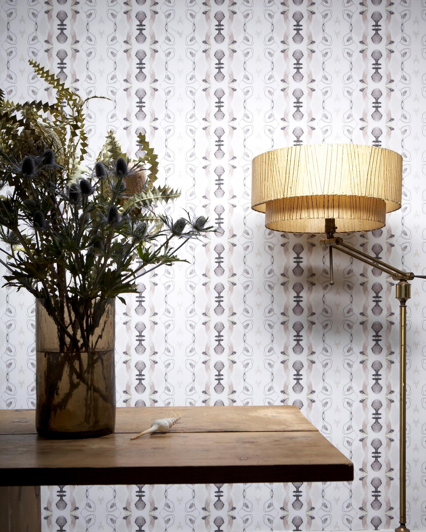 A table with a Bali Stripe Wallpaper Sand and a lamp in front of it, showcasing the abstract aesthetic