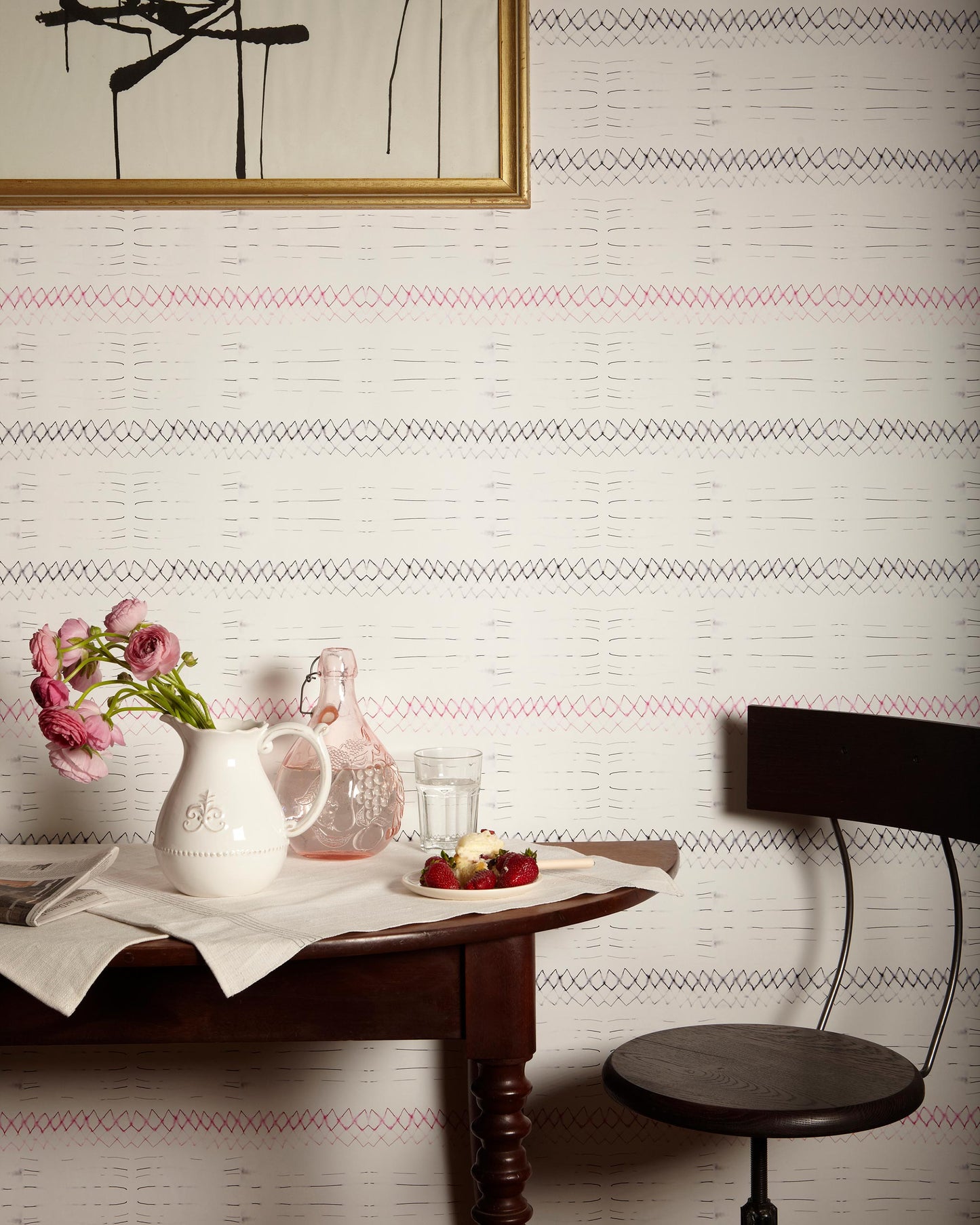 A table with a vase of flowers and a Native Stripe Wallpaper Black + Crimson fabric covering
