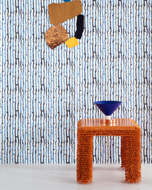 A table with an orange stool in front of a blue Drippy Stripe Wallpaper Azure fabric