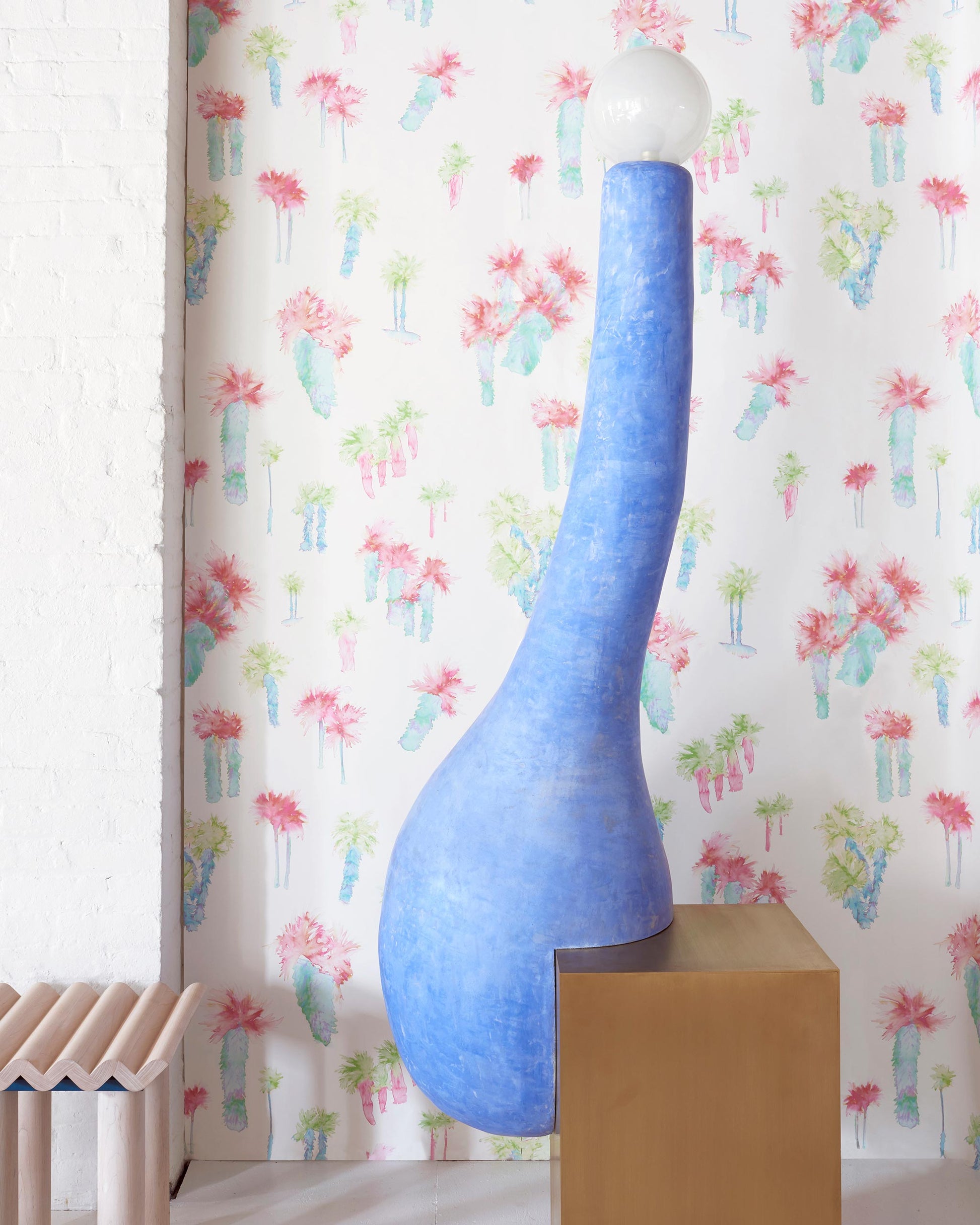 A blue vase sits on a wooden table in front of Perfect Palm Wallpaper Polychrome wallpaper