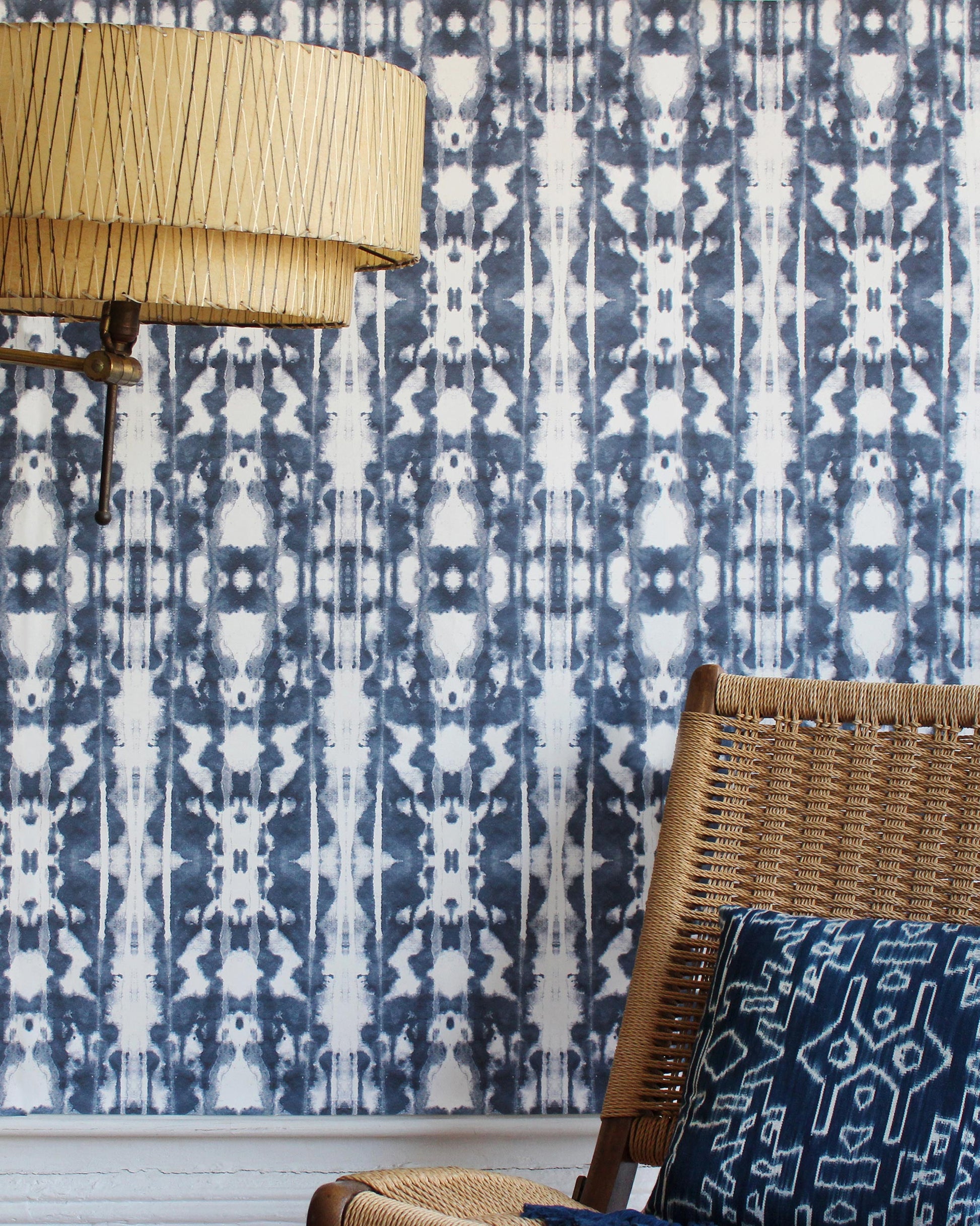 A wicker chair in front of a blue and white luxury Biami Wallpaper with the Nila pattern