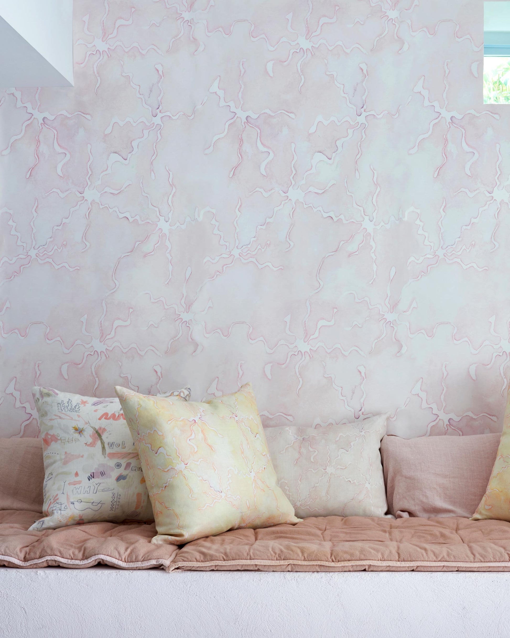 A bed with pillows and a pink wall, featuring Pecosa Wallpaper Light Peach design accents