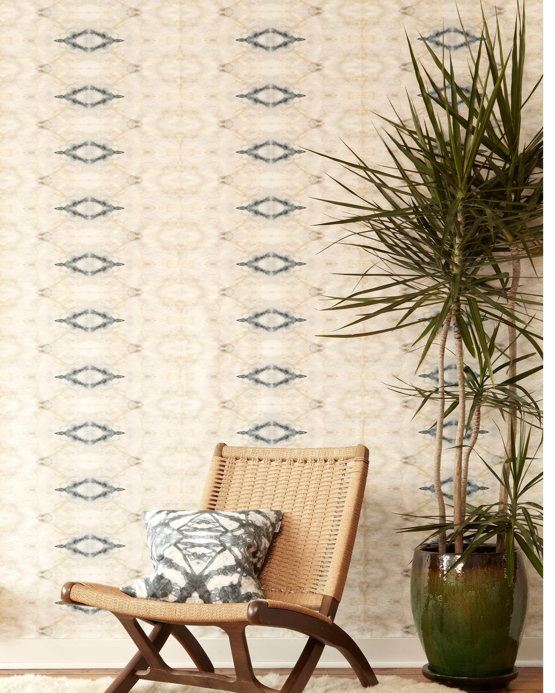 A chair and a potted plant in front of The Knitting Wallpaper Sand luxury wallpaper