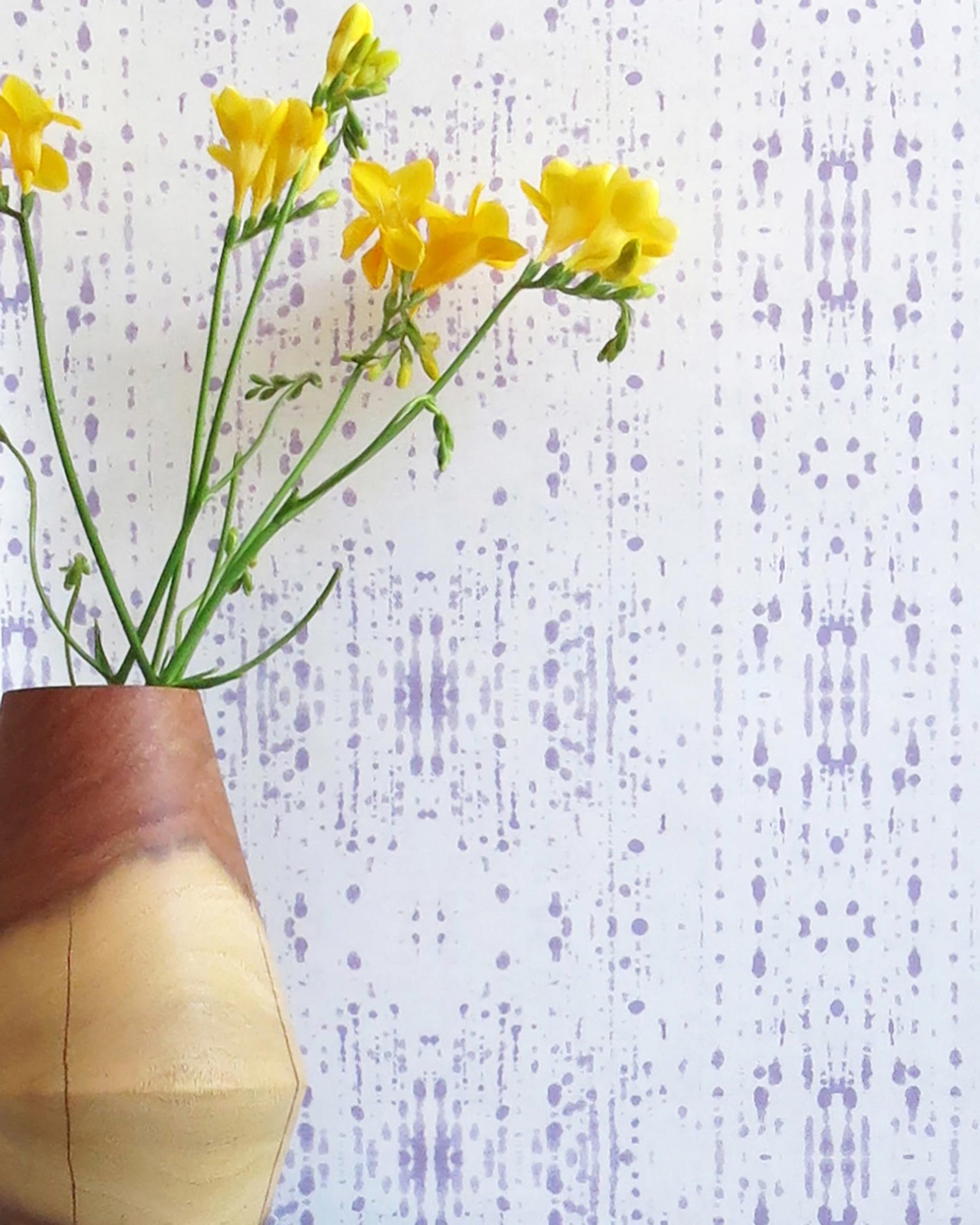A vase of yellow flowers in front of a purple Omaha Kinship Wallpaper || Mulberry.