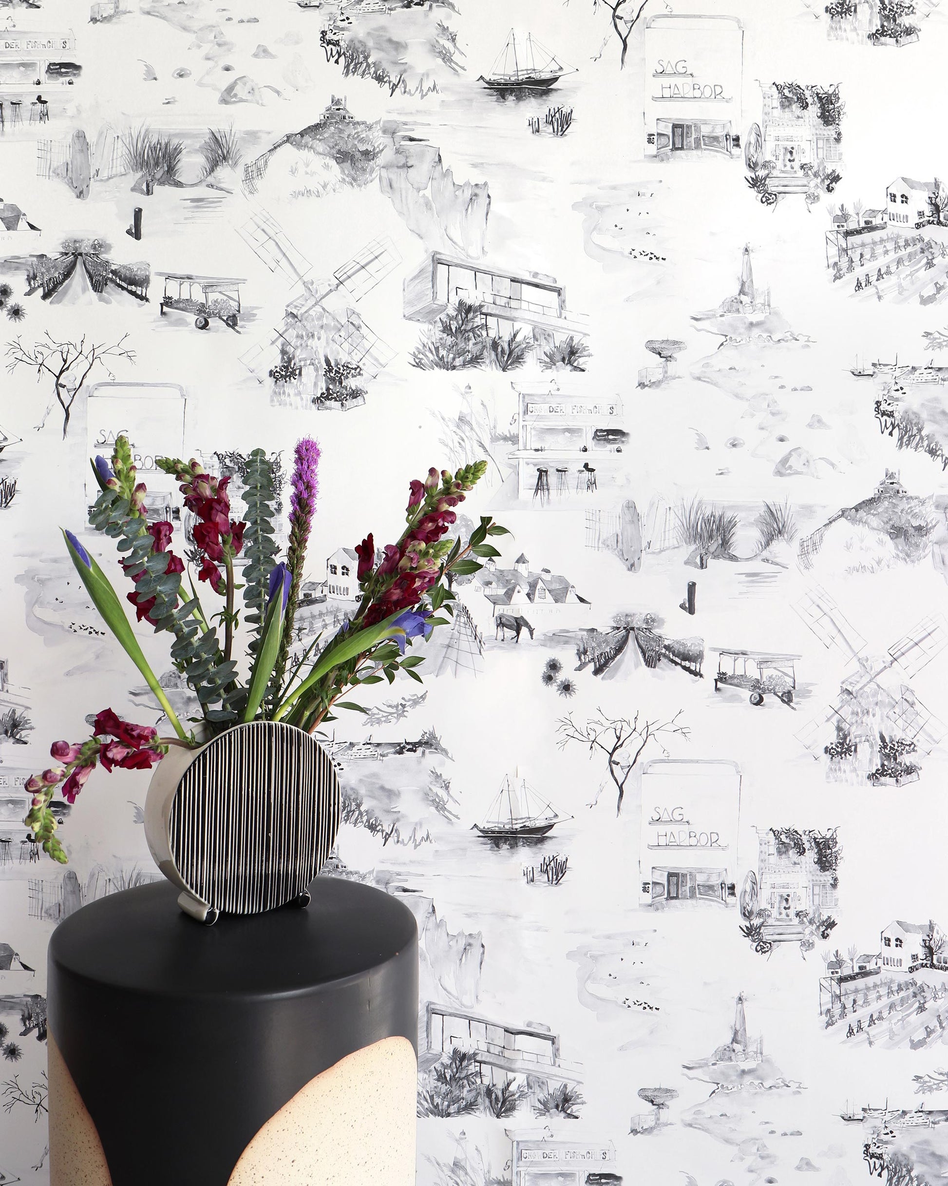 A black and white luxury fabric with a modern toile pattern, featuring the Out East Wallpaper Greyscale in front