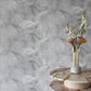 A marble table with a vase in front of it, showcasing a Palmeti Wallpaper Alba fabric pattern
